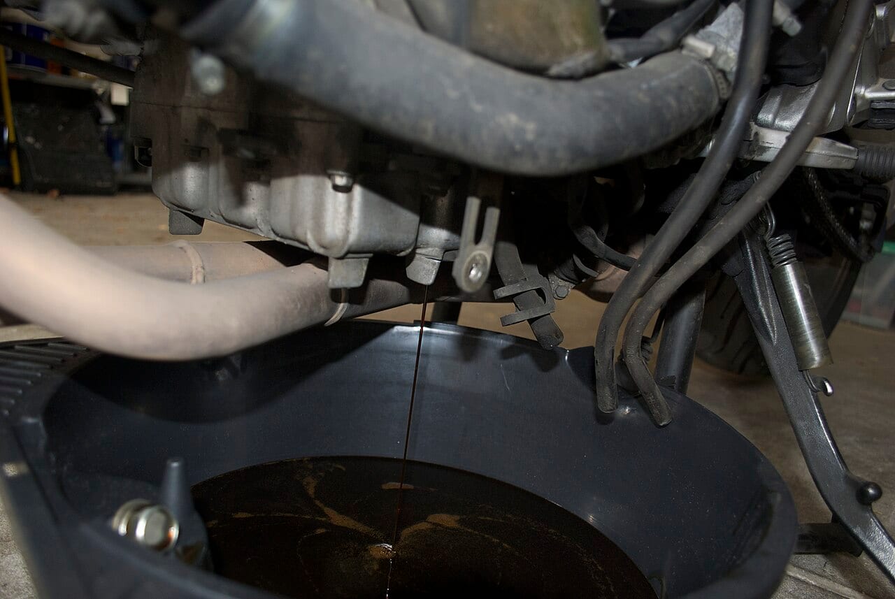 Aceite usado drenando del cárter de una moto Honda hacia un recipiente durante un cambio de aceite
