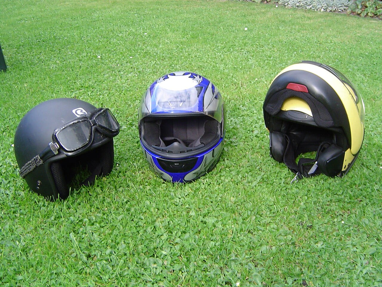 Tres cascos de moto sobre el pasto: uno abierto tipo jet, uno integral y uno modular (foto: Piero at Dutch Wikipedia, CC BY-SA 3.0, Wikimedia Commons)