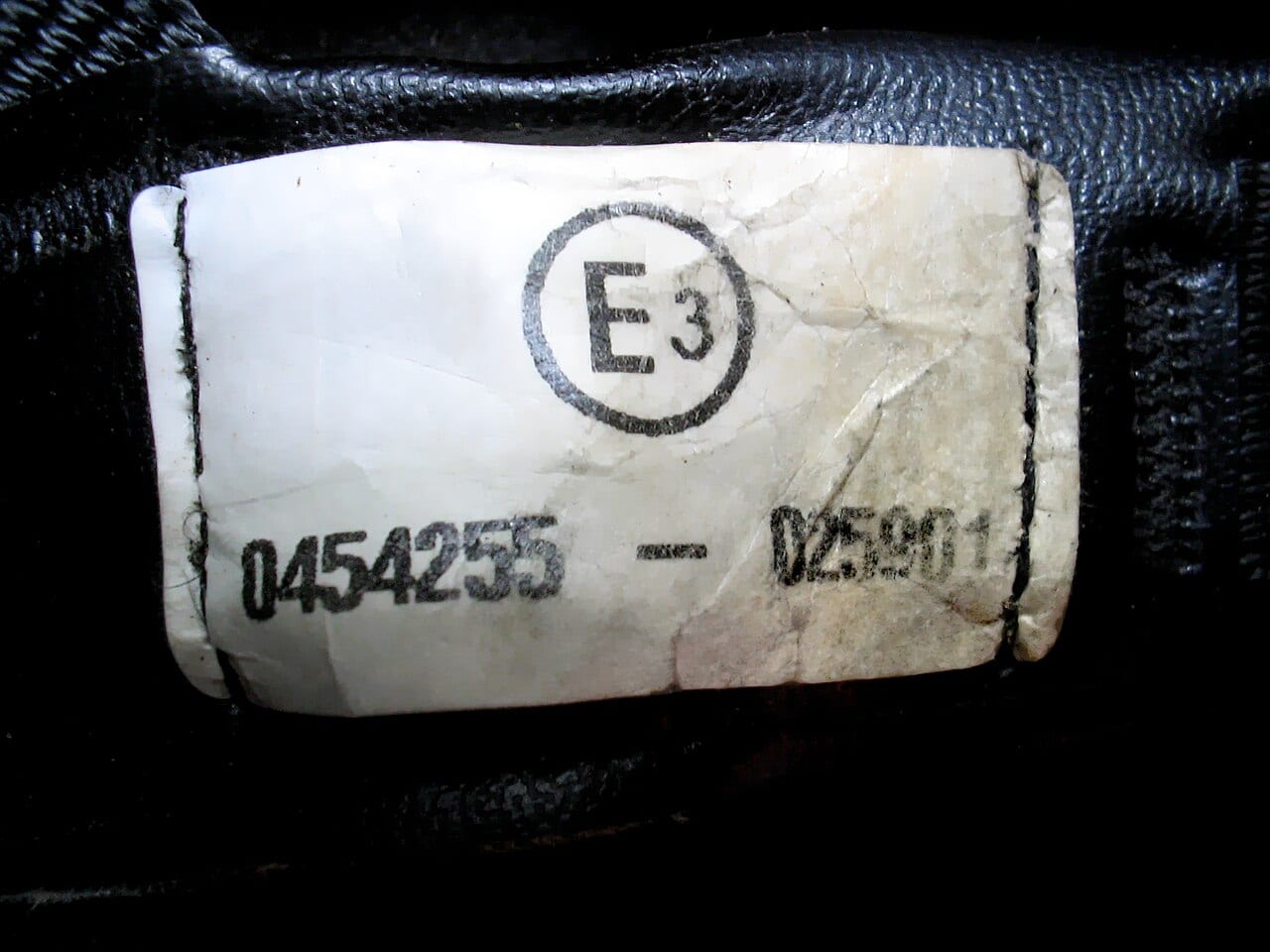 Etiqueta de homologación ECE cosida en la correa de un casco de moto, con la letra E dentro de un círculo y el número de aprobación