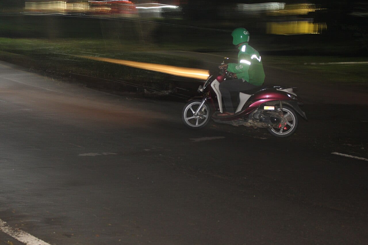 Motociclista con casco circulando de noche por una vía oscura, con la luz delantera encendida (foto: Oktafialni, CC BY-SA 4.0, Wikimedia Commons)