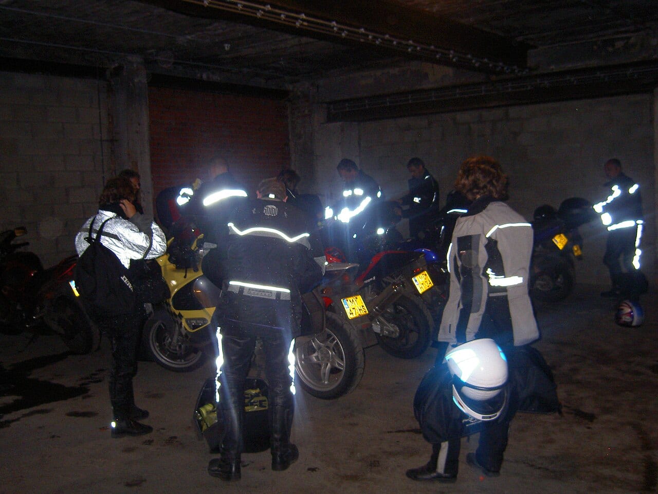 Grupo de motociclistas de noche con chaquetas y pantalones con bandas reflectivas que brillan con el flash
