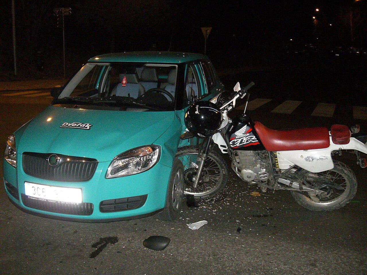 Choque entre un carro y una moto en un cruce, con la moto apoyada contra el frente del vehículo